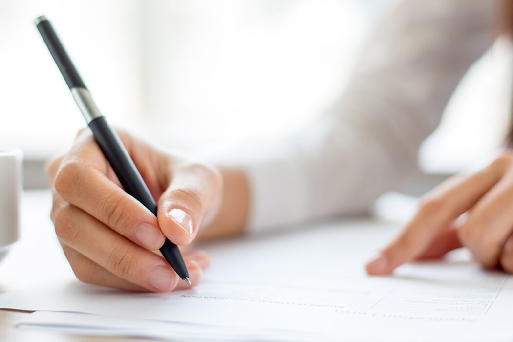 A tight shot of a woman's arm as she writes a note on a piece of paper with a pen.