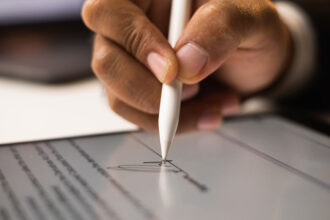 Close up of a black man signing a digital document on a tablet.