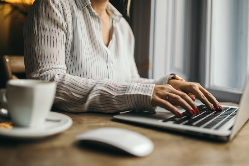 A person typing at a laptop with a mouse and a mug beside them