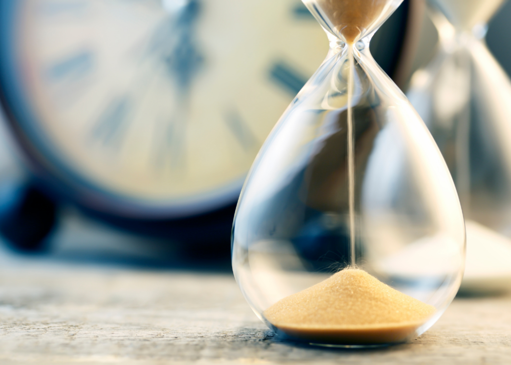 An hourglass with a clock in the background